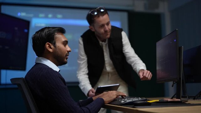 A standing team lead and a seated engineer open their hands toward each other as the run finally comes back clean inside a dimly lit machine learning startup office.