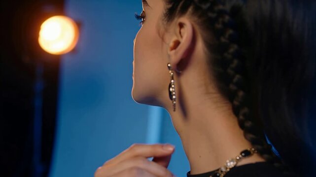 Touching model adjusting teardrop earring in studio warm lamp, layered necklace
