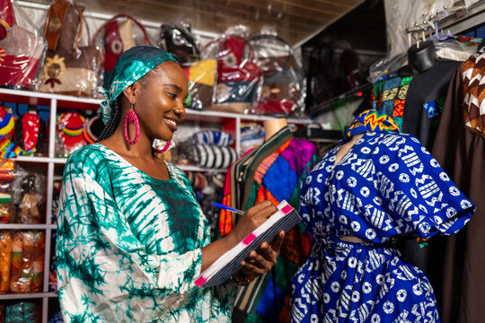 African woman small business owner checking inventory in her fashion store using notebook,SME