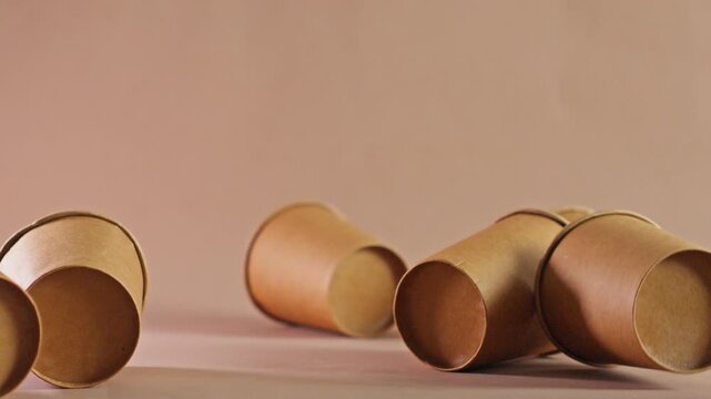 Eco-friendly brown kraft paper cups falling down and scattering on beige background in slow motion