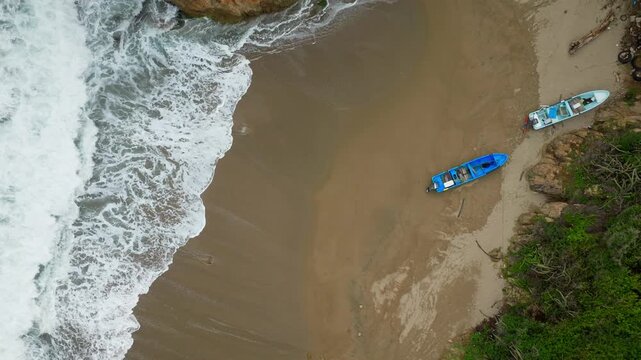 Two small boats rest on sandy Bejuco Beach by breaking surf in Costa Rica, aerial static as water rushes along shores