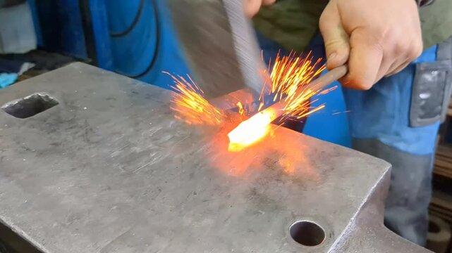 A skilled metalworker uses traditional blacksmithing techniques to shape a glowing hot iron rod on a heavy steel anvil using a hammer and tongs in an industrial workshop environment

