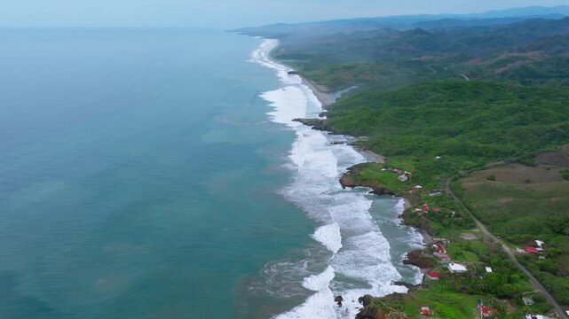 Long tropical coastline with breaking waves, green hills and scattered homes, aerial panoramic above Bejuco Costa Rica