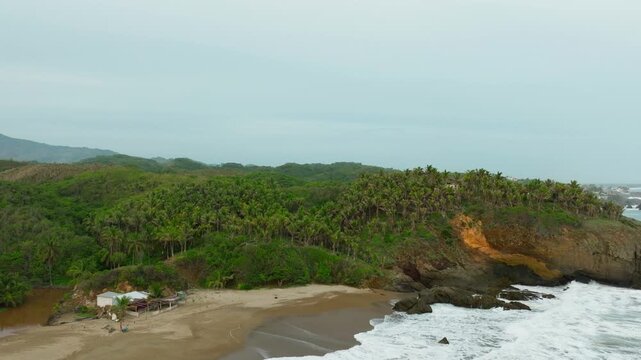 Tropical Bejuco Beach meets rocky headland and dense palms on Costa Rica coast, aerial establishing dolly