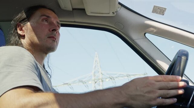 Close passenger-side view of male driver holding steering wheel with both hands inside car cabin, dashboard visible, natural daylight through window, seatbelt and seat controls visible