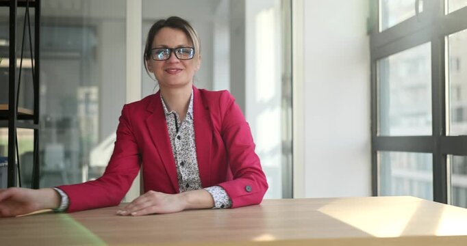 In a bright and modern office, a woman in a red jacket sits at a wooden table. She playfully interacts with crumpled paper, embracing the creative process while smiling.