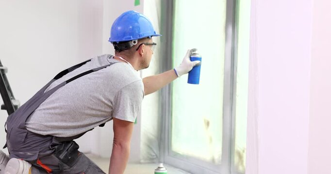 A skilled worker applies vibrant blue spray paint to window frames in a light-filled space. The atmosphere buzzes with creativity and determination.