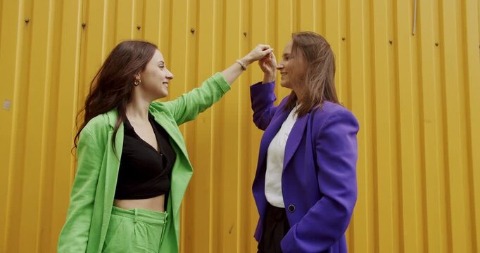 Young woman hugging and kissing happy girlfriend. Love and kiss, LGBTQI, LGBT Pride Month, friendship concept. LGBT Female talking and dancing in colorful clothes outdoors on wellow background.