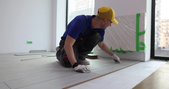 A skilled worker carefully lays down elegant flooring in a bright apartment. Each plank is placed with precision, enhancing the room's charm and allure.