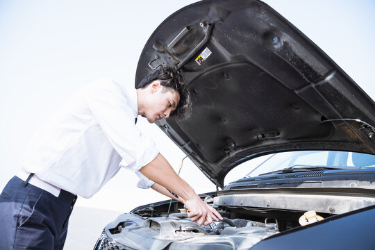 Man inspecting car engine under open hood outdoors