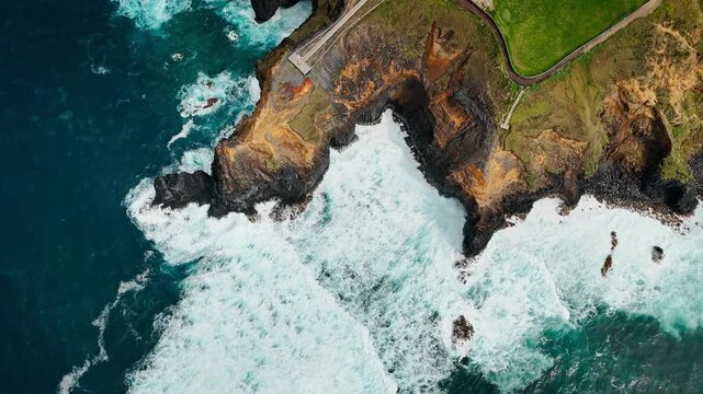 Close aerial view of Atlantic waves striking base of basalt cliffs. Ocean swell, breaking waves and white sea foam