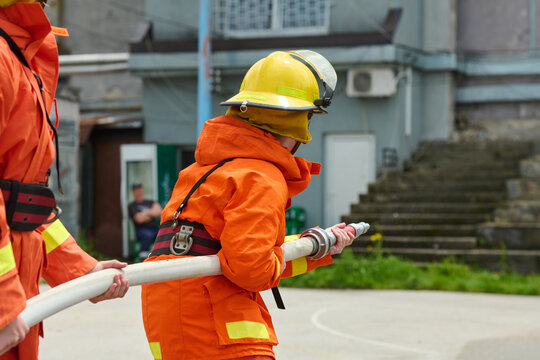 Firefighter Team Working With Hose During Outdoor Training Drill Wearing Orange Protective Gear And Helmet