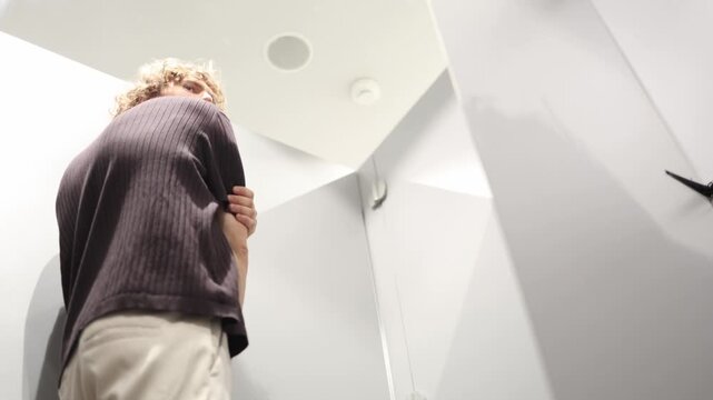 Man checks how his T shirt fits while trying on clothes studying fit comfort and overall look in the mirror before deciding whether a new style suits him and is worth it