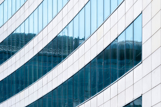 Curved modern facade with blue windows and white horizontal bands creates an abstract pattern in architecture where glass and structure repeat across the frame