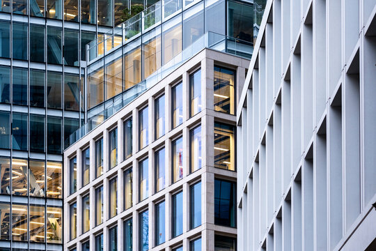 Modern buildings with glass windows and white facade elements create layered urban architecture where offices and structural lines overlap across the frame