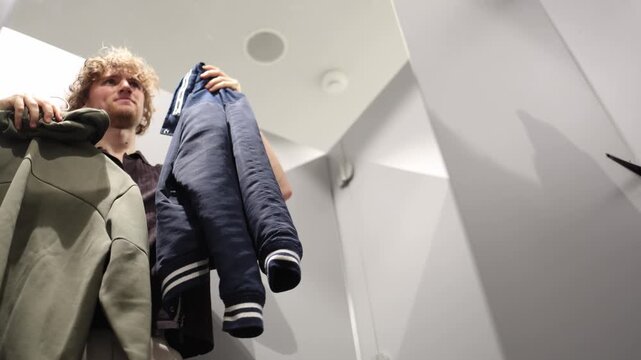 Man compares two clothing options before buying carefully checking their look style and suitability while deciding which item is the better choice for his wardrobe to buy