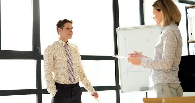 Two colleagues work together in a sunlit office, sharing ideas and insights while standing near a whiteboard. Their dynamic exchange fosters creativity and collaboration.