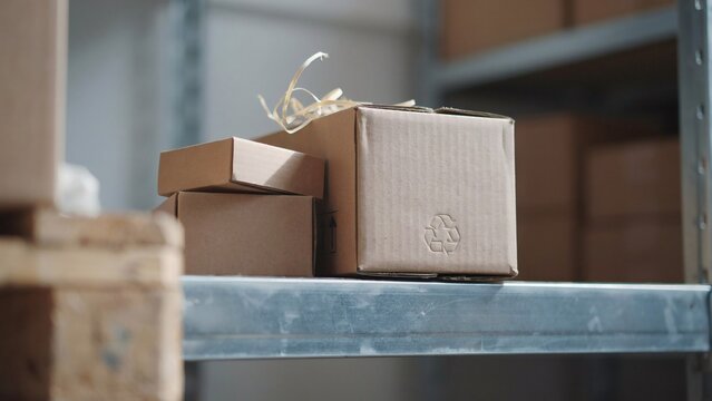 Cardboard boxes with a recycling symbol sitting on a metal shelf in a warehouse with several brown cardboard recycling logo arranged storage shelf inside