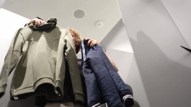 Man compares both clothing options in a fitting room and struggles to decide what to choose while weighing style comfort and the best look before making a purchase choice