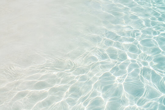 Clear blue water surface with sunlight reflections over light sand
