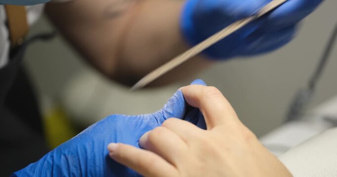 A talented technician shapes fingernails in a modern salon, focusing on detail and skill. Blue-gloved hands expertly use a file, creating a perfect manicure.