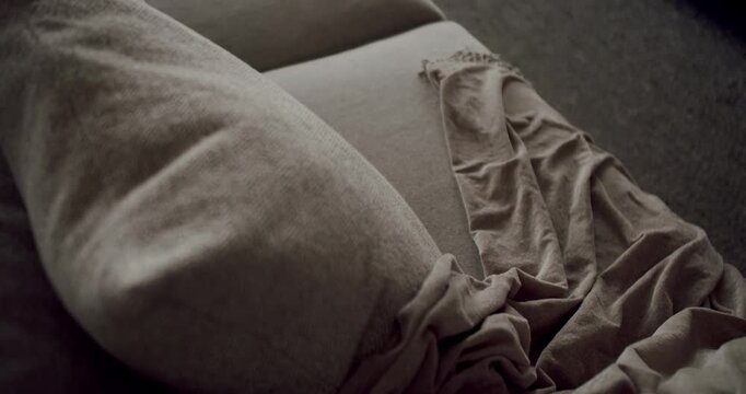 A detailed close-up image showcasing the texture and fabric of a grey couch with a wrinkled throw blanket. Neutral Colored Couch with Textured Pillows and Throw in Room.