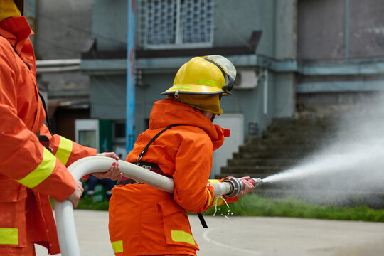 Firefighters Training With Hose Spraying Water During Urban Firefighting Drill And Safety Exercise