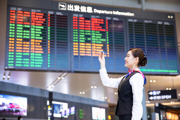 Smiling flight attendant pointing at airport departure board © DaoBaoTran