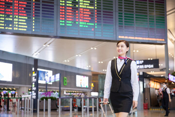 Female flight attendant pulling suitcase at airport with departure board © DaoBaoTran