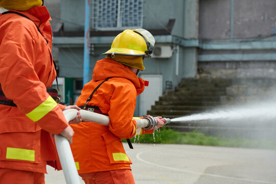 Firefighters Working Together With Hose During Firefighting Training Wearing Orange Protective Gear And Helmets