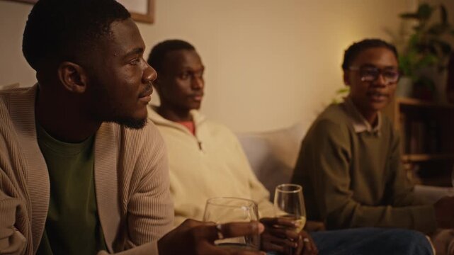African American young adults sitting together holding wine glasses, conversing during holiday gathering. Footage suitable for friendship, beverage marketing, lifestyle campaigns