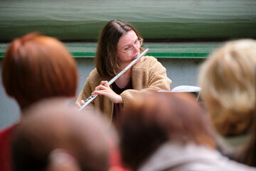 Woman musician playing flute during outdoor rehearsal in front of blurred audience. Flutist performing classical music at open air concert. Street performance and live music concept © Андрей Журавлев