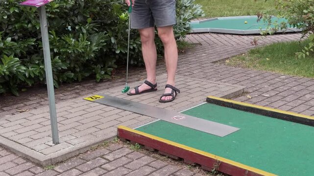 Man playing mini-golf outdoors, preparing to hit ball on putting green course