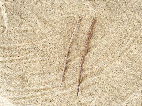 Two small wooden sticks placed parallel on a textured sand background.