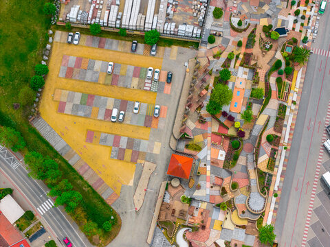 Aerial view of a parking lot and a display area featuring various colorful paving stone samples with a red-roofed structure and surrounding trees in Otnice, South Moravian Region, Czechia.