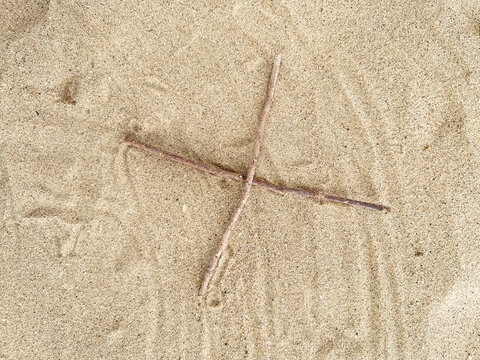 Two wooden sticks crossed in an 'X' shape on a textured sand surface.