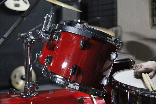 A person plays a beat on a red drum kit using wooden drumsticks.