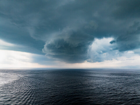 Aerial view of dark, heavy storm clouds gathering over the turbulent sea with dramatic lighting near the coast of Nusa Penida, Bali, Indonesia.