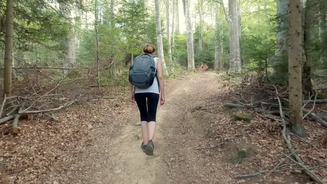 Fit senior woman carrying a backpack, in great shape and excellent physical condition, hiking on the mountain path. Concept of active aging and healthy lifestyle. 