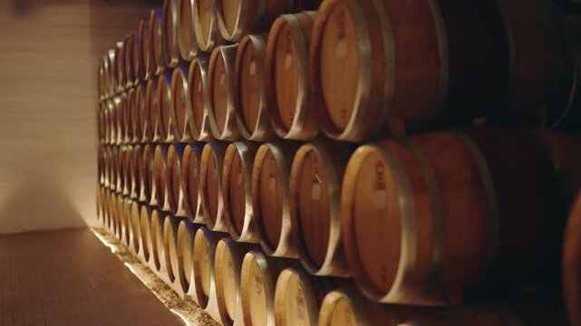 Numerous wooden barrels stacked in rows inside a traditional wine cellar for aging alcoholic beverages, showing the long process of fermentation and winemaking in a rustic warehouse