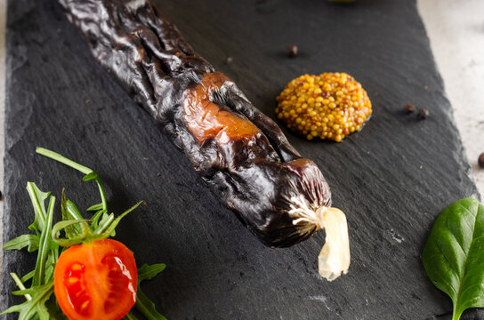 Dry cured sausage with cherry tomatoes, green olives and mustard on black slate