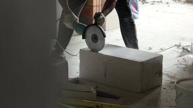 Worker cutting concrete block with angle grinder during construction