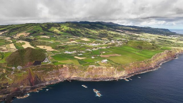Farmland along volcanic cliffs on Sao Miguel, Azores, Portugal. Aerial view across patchwork fields and rural coastal landscape overlooking Atlantic Ocean on green island.