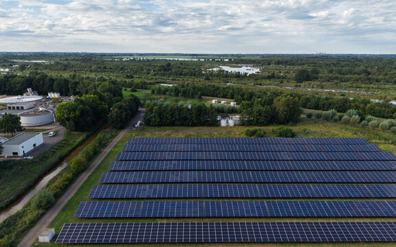 Aerial view of a solar panel farm next to the Waterschap Amstel, Gooi en Vecht water treatment facility, surrounded by green fields in Nederhorst Den Berg, Noord-Holland, Netherlands.