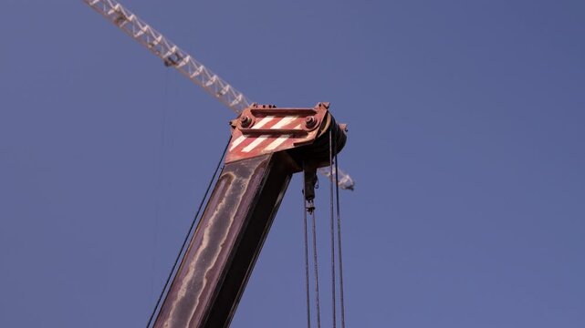 Mobile crane boom lifting cables against clear blue sky