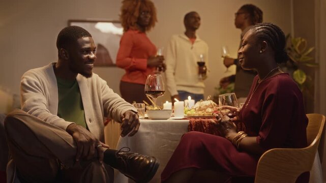 Young adult African American man and woman talking at Thanksgiving dinner while friends mingle. Clip fits festive holiday marketing campaigns and friendship lifestyle advertising