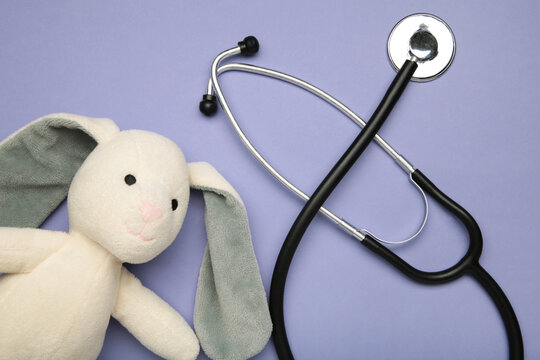 Pediatrician concept. Toy bunny and stethoscope on purple background.
