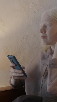 Pretty albino woman texting with smart phone using social media network relaxing in comfortable couch in stylish living room. People and gadget concept.