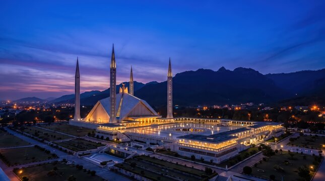 Majestic evening view of Faisal Mosque illuminated beneath a deep blue twilight sky with surrounding city lights and mountains.
