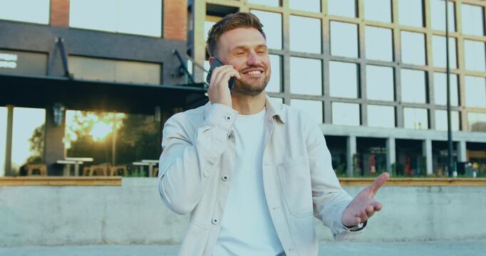 Smiling businessman sitting on an outdoor terrace during lunch break, talking on smartphone, drinking coffee and typing on laptop.